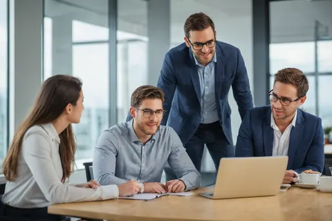 Four business professionals collaborating around a laptop in a modern office with large windows.
