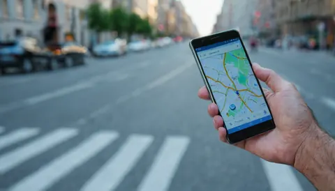 Hand holding smartphone with map app open on city street with crosswalk and cars