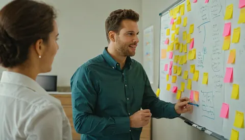 Man and woman collaborating at a whiteboard with sticky notes in an office