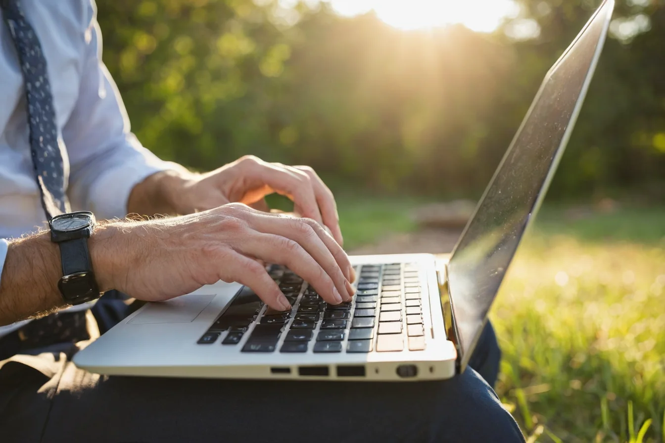Man in business attire typing on laptop outdoors in golden sunlight