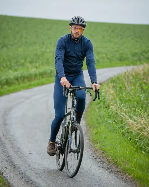 Man riding bicycle on rural gravel road surrounded by green fields