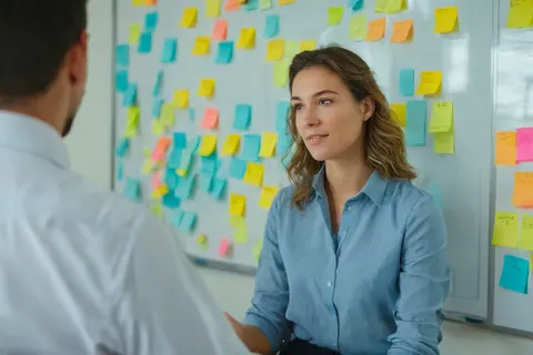 Two people in an office discussing ideas with colorful sticky notes on a whiteboard.