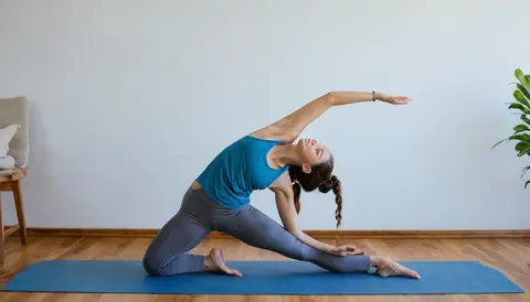 Woman stretching on blue yoga mat in minimalist room with wooden floor and green plant